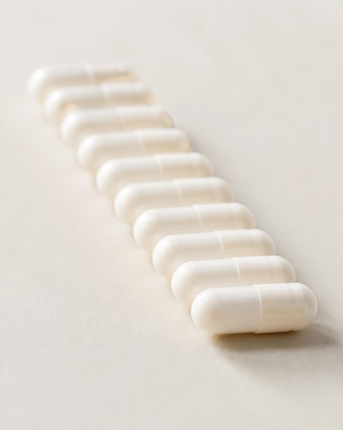 Plain white inert capsules arranged in a precise row on a warm off-white surface